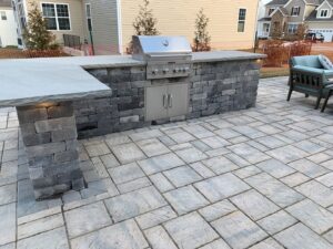 Gray paver patio in backyard with outdoor BBQ area and seating